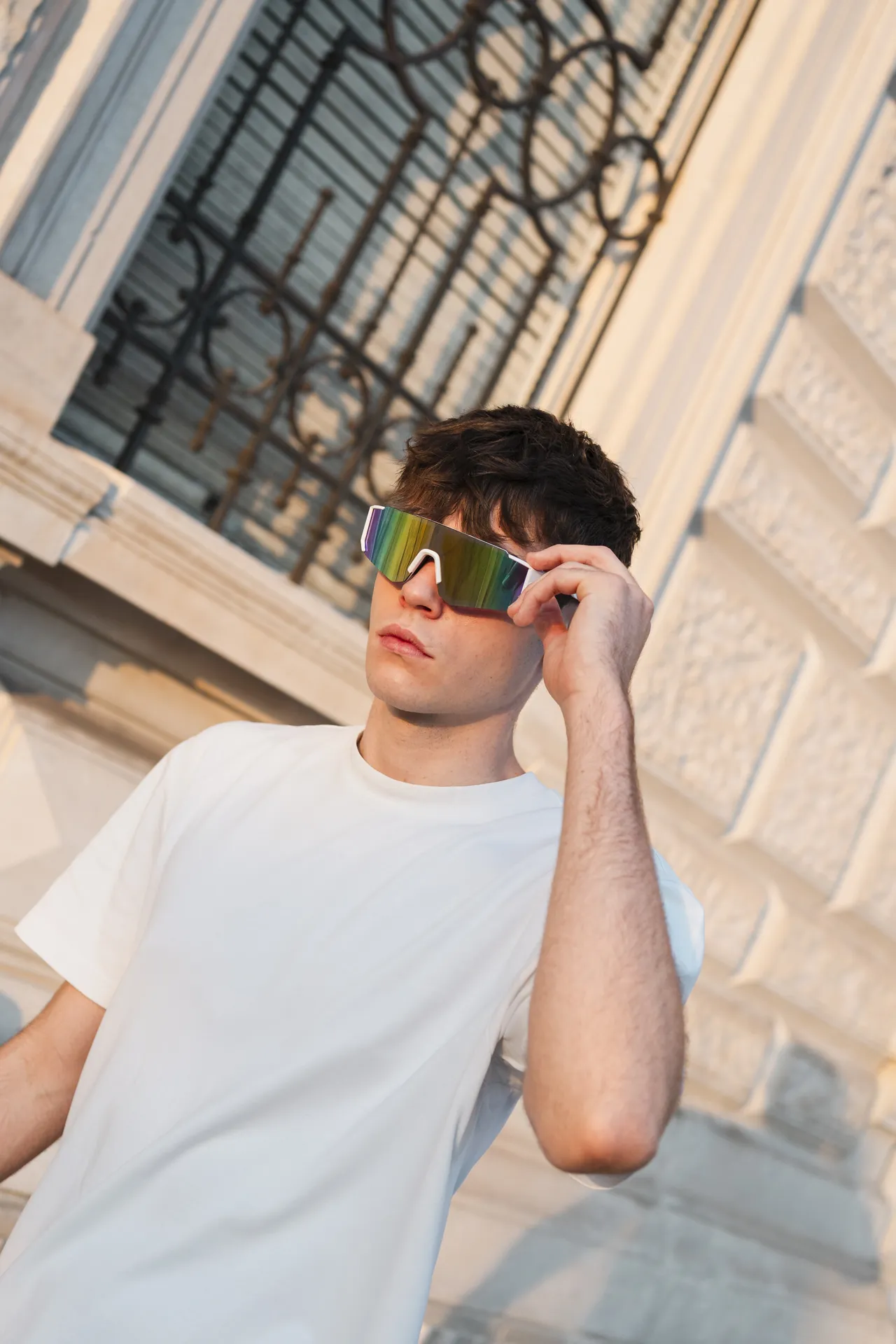 Modello che sistema gli occhiali sportivi Blank a specchio davanti a un palazzo storico di Trieste